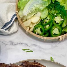 two plates filled with meat and vegetables on top of a white tablecloth next to a bowl of green peppers