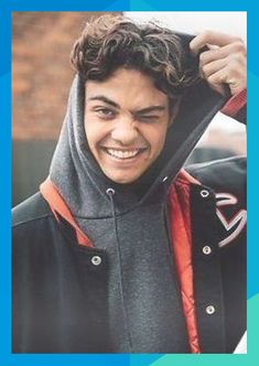 a young man is smiling while wearing a hoodie and holding his jacket over his head