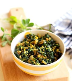 a bowl filled with spinach and corn on top of a wooden cutting board