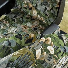 an upholstered chair with green and brown floral fabric on the seat, in front of a carpeted floor