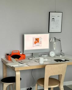 a desk with two chairs and a computer monitor on it, in front of a gray wall