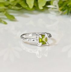 Show your love with this exquisite Peridot ring. Handcrafted in wax and cast in Solid Silver, this stunning green crystal ring features an organic textured band, ensuring its uniqueness. Adorned with a mesmerizing princess-cut Peridot, also the August birthstone, it embodies more than an engagement ring - it symbolizes timeless love and individualityT H E ∙ S M A L L ∙ D E T A I L S• Princess-cut Peridot (5 x 5mm)• Sterling Silver textured bandM A T E R I A L ∙ O P T I O N S• Sterling Silver• So Peridot Wedding Ring Silver, Peridot Ring Silver, Silver Peridot Ring, Silver Peridot Round Rings, Silver Peridot Solitaire Ring, Silver Peridot Rings Fine Jewelry, Green Crystal Ring, Silver Peridot Gemstone Ring, Timeless Love