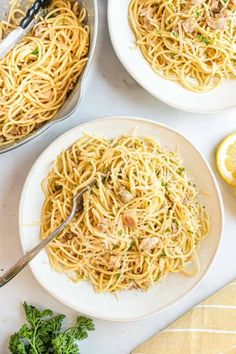 three plates of pasta with chicken and parsley on the side, next to lemon wedges