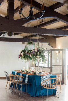 a dining room table with blue linens and flowers hanging from it's ceiling