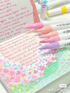 several pens are lined up in front of an open book with writing on the pages