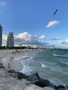 people are on the beach and in the water near buildings with high rise skyscrapers