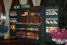 a display case filled with candy and candies in front of a brick wall that reads news stand