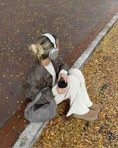 a woman sitting on the ground with headphones in her ears and holding a camera