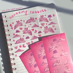 a notebook with pink stickers on it next to a spiral bound book and pen