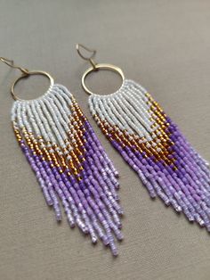 two pairs of beaded earrings with gold and purple beads hanging from hoops on a gray surface