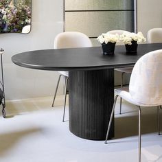 a black table with white chairs and vases on it