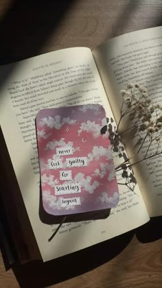 an open book sitting on top of a wooden table next to a vase with flowers