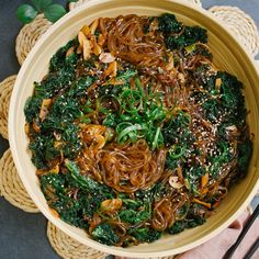 a bowl filled with noodles and greens on top of a table