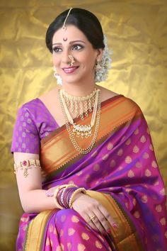 a woman in a purple and gold sari with jewelry on her neck, smiling