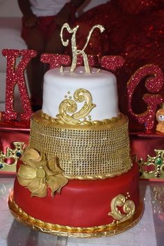 a red and gold cake with the letter k on it's top is sitting on a table