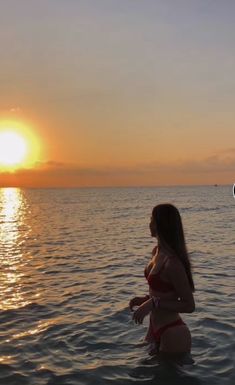 a woman standing in the water at sunset