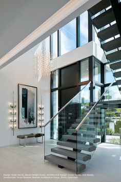 an elegant staircase with glass railing and chandelier in the middle of a room