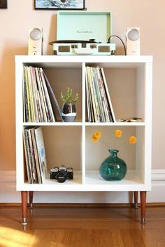 an old record player sits on top of a white shelf next to a vase with yellow flowers