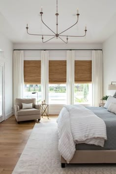 a large bed sitting under a window next to a white chair in a living room