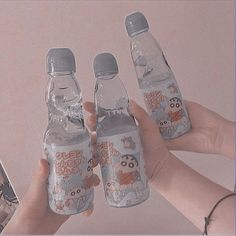 three water bottles with animals on them being held by two hands