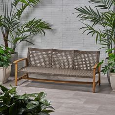 a wooden bench sitting next to potted plants on a tiled floor in front of a white brick wall