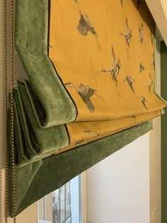 a green and yellow roman blind with birds on it hanging in front of a window