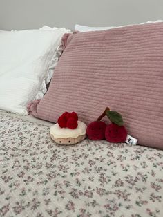 two stuffed cherries sitting on top of a bed next to pillows and pillow cases