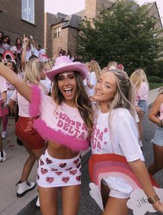 two women in pink and white outfits are posing for the camera with other people behind them