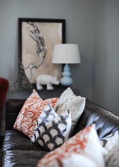 a living room filled with lots of pillows on top of a brown leather couch next to a lamp