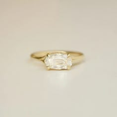 a yellow gold ring with an oval cut diamond in the center, on a white surface