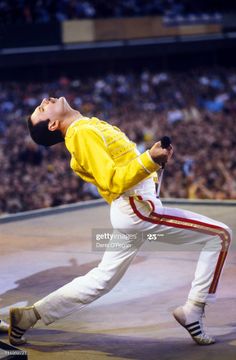 a man in yellow shirt and white pants performing on stage with crowd watching from the stands