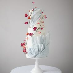 a three tiered white cake with flowers on top and blue fabric draped over it