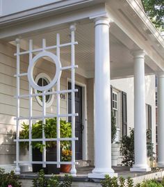 a house with white columns and a clock on the front door, surrounded by plants