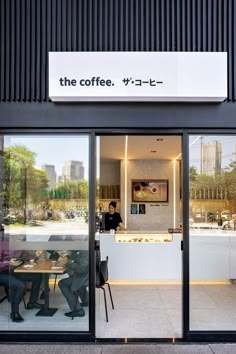 people sitting at tables in front of a coffee shop with large glass doors that open to the outside