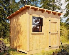 a small wooden shed sitting in the middle of a field with trees and grass around it