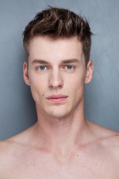 a shirtless man with blue eyes and no shirt is posing for the camera in front of a gray wall