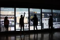 three people standing in front of a wall that has pictures on it and one person pointing at them