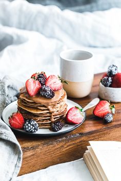 a stack of pancakes with chocolate frosting and fresh berries on the side next to a cup of coffee