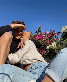 a man and woman sitting on the ground with their arms around each other as they kiss