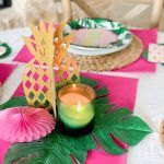 the table is set with pink and green plates, napkins, and pineapple centerpieces