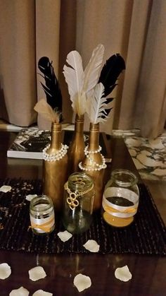 there are three bottles with feathers in them on the table next to some candles and pearls