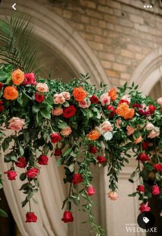 an arrangement of flowers hanging from the ceiling in front of a brick building with arched doorways