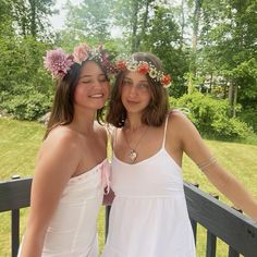 two young women standing next to each other on a deck with trees in the background