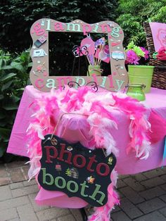 a photo booth with pink and green decorations on the table in front of some trees