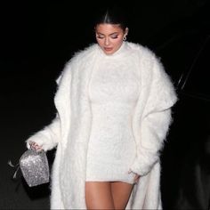 a woman is walking down the street wearing a white coat and high heeled shoes