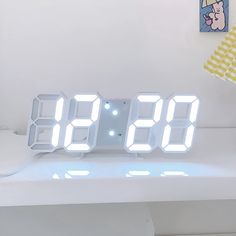 an alarm clock is sitting on top of a white table next to a yellow lamp