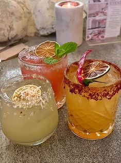 three different types of cocktails sitting on a table next to each other, one is orange and the other has a garnish