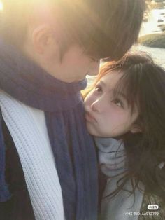 a man and woman kissing each other on the street in front of some water with sun flares behind them