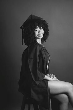 a black and white photo of a woman wearing a graduation cap sitting on a stool