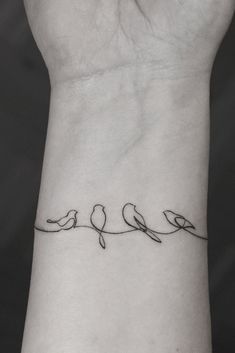 a small wrist tattoo with birds on the line and two smaller birds sitting on top of each other